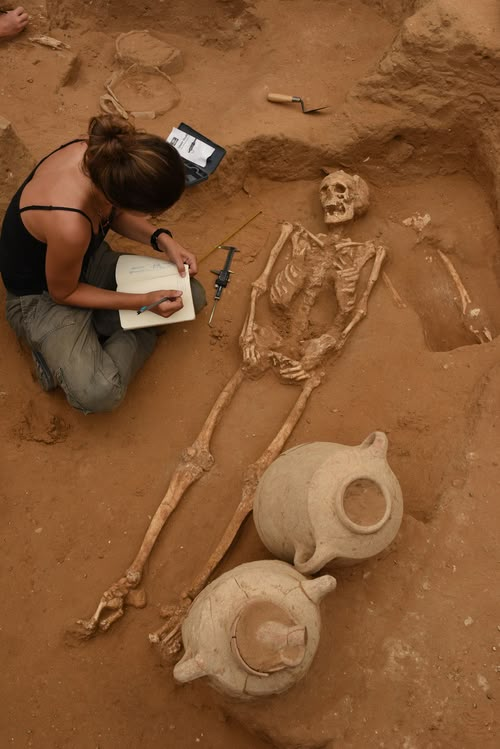 a woman sitting on the ground next to two skeletons