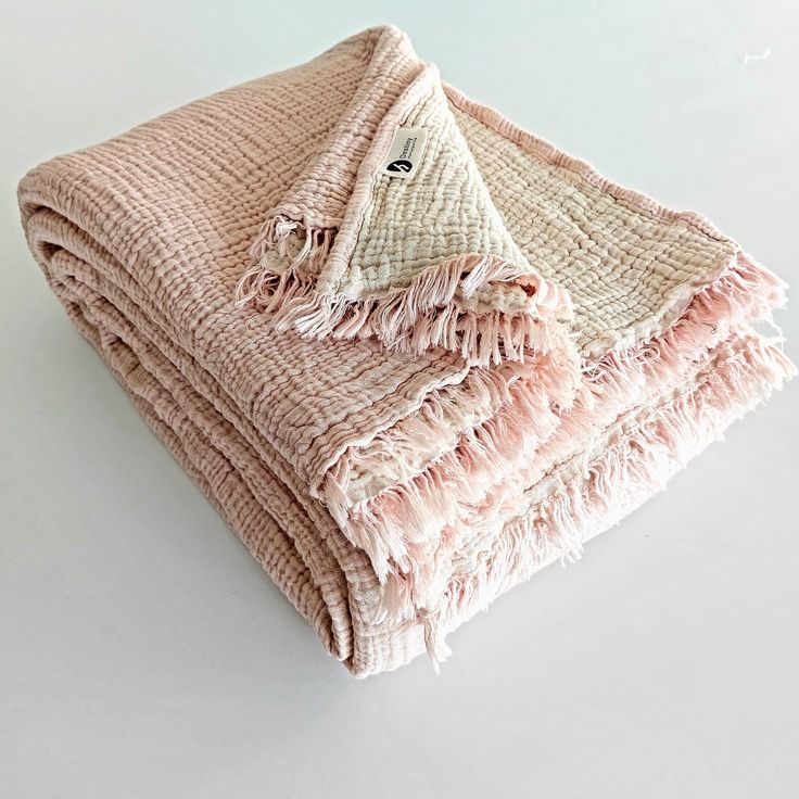 two blankets folded on top of each other with pink and white fringed edges, sitting next to each other