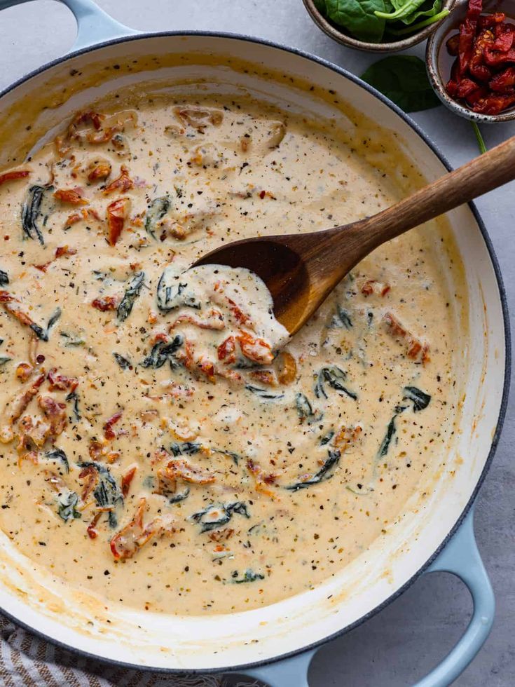 a wooden spoon in a pot filled with cream sauce and spinach on the side