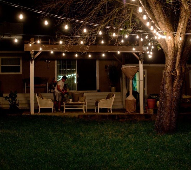 the patio is lit up at night with string lights strung over it and two people sitting outside