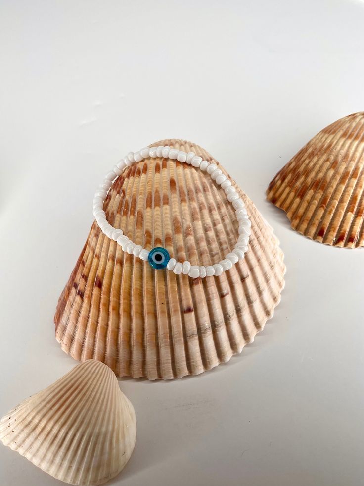 two seashells with a blue evil eye beaded necklace on them and one shell is laying next to it