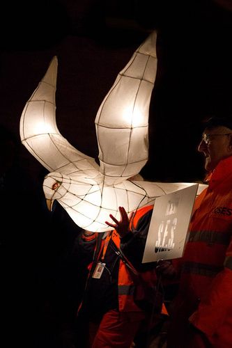 a man in an orange jacket holding a white paper bird with lights on it's wings