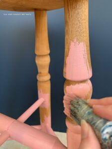 someone is painting the legs of a wooden chair with pink and blue paint on it