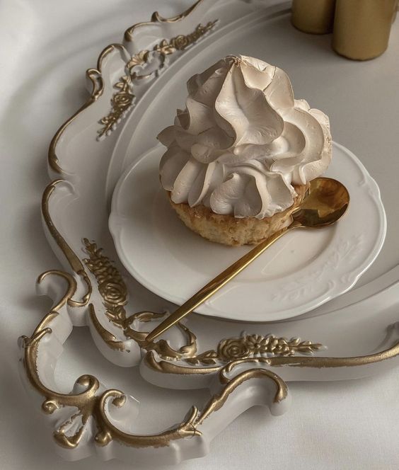 a white plate topped with a pastry covered in whipped cream next to a gold spoon