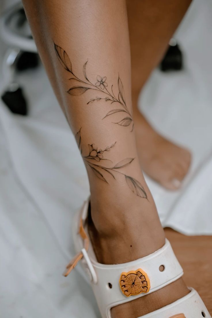 a woman's foot with tattoos on it and white sandal sandals in front of her