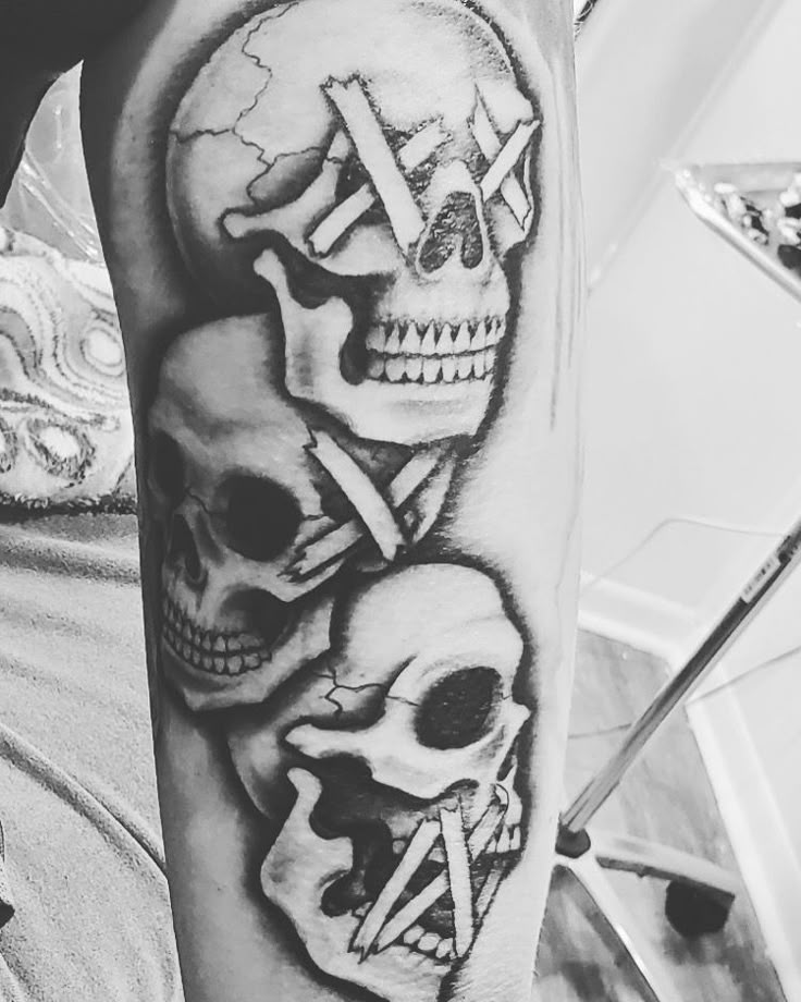 black and white tattoos on the arm of a man with two skulls in front of him