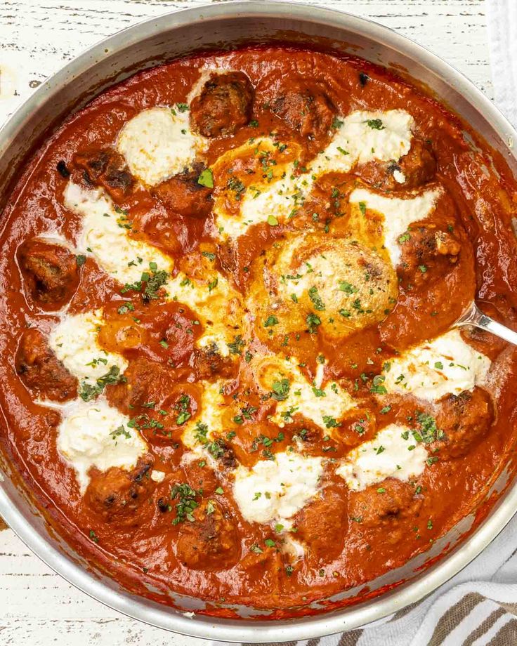 a metal pan filled with meatballs and cheese on top of a white table cloth