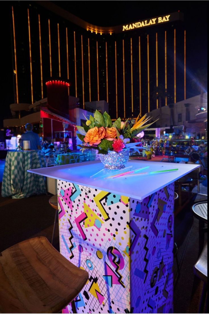 a table with flowers on it in front of a neon sign and building at night