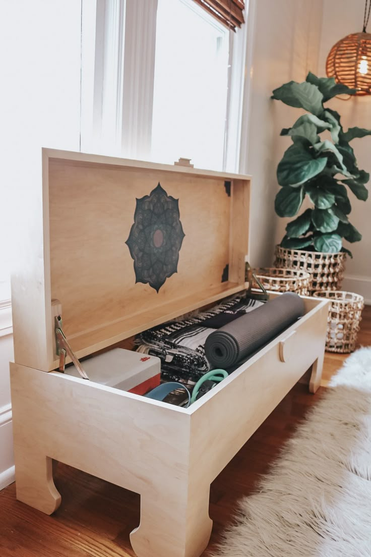 an open wooden box sitting on top of a hard wood floor next to a potted plant