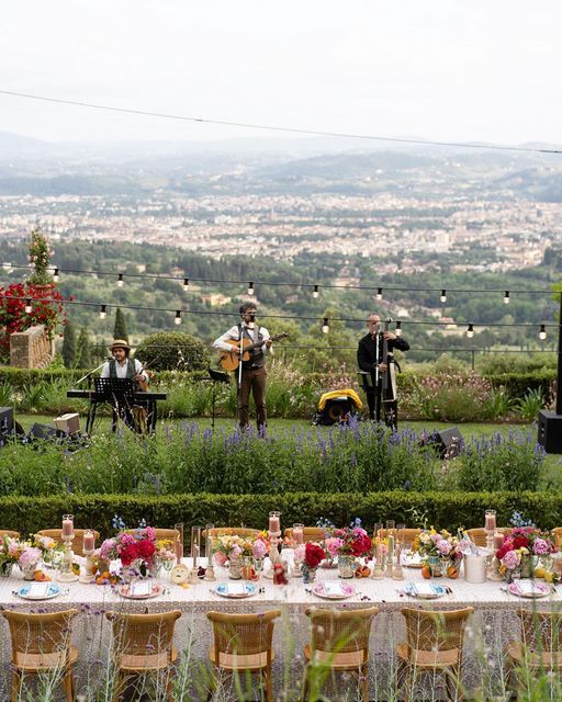 an outdoor dinner table set up in the middle of a field with people playing instruments