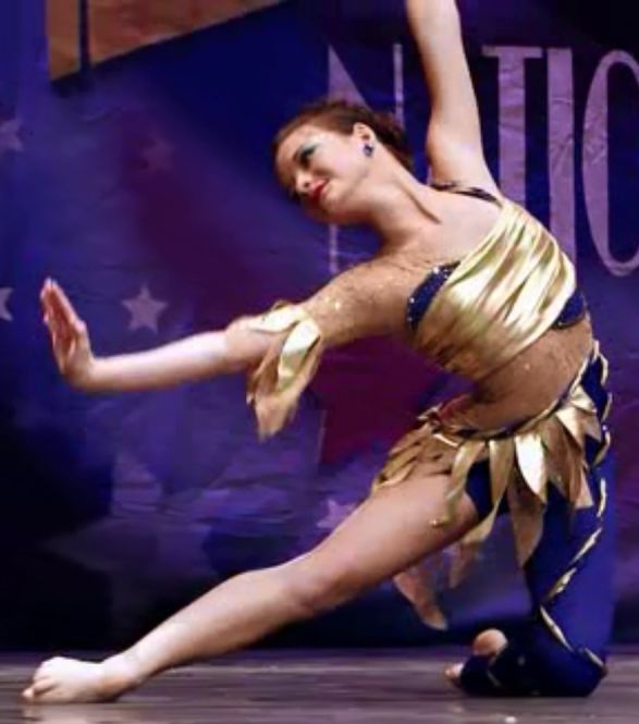 a woman in a gold and blue dress is doing a dance move with her legs spread out