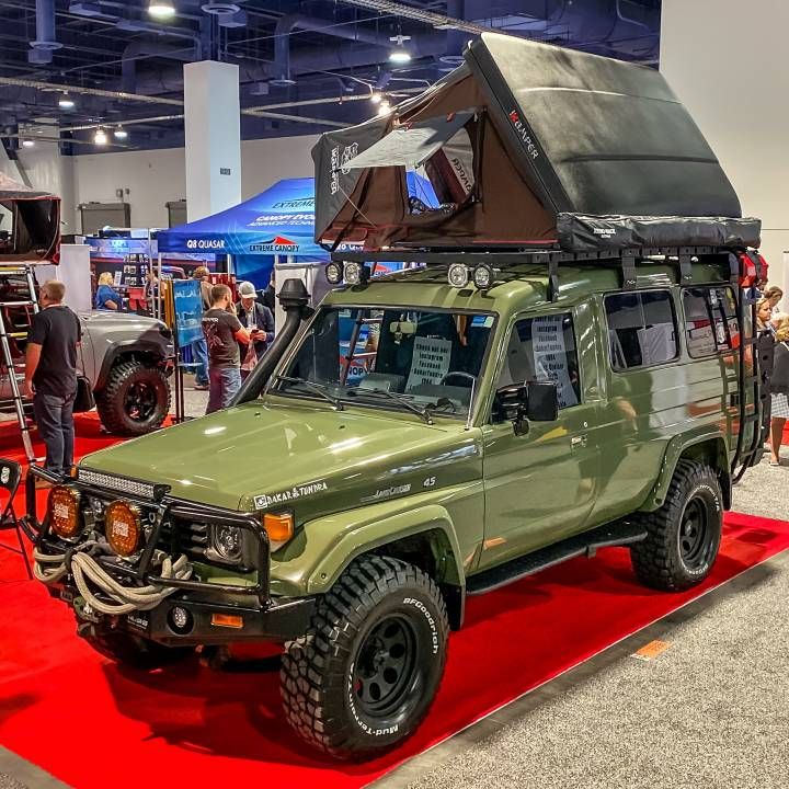 a green truck with a tent on the roof and people standing around looking at it