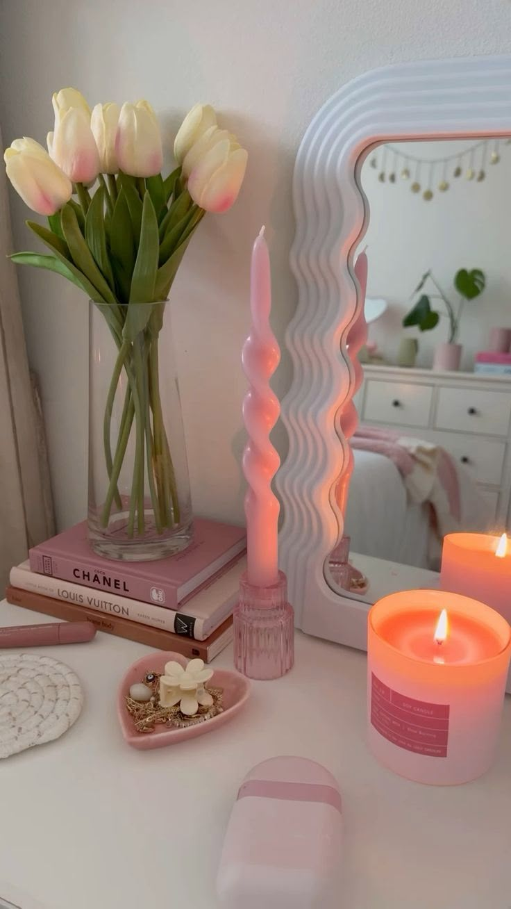 a white table topped with pink candles and other items next to a vase filled with flowers