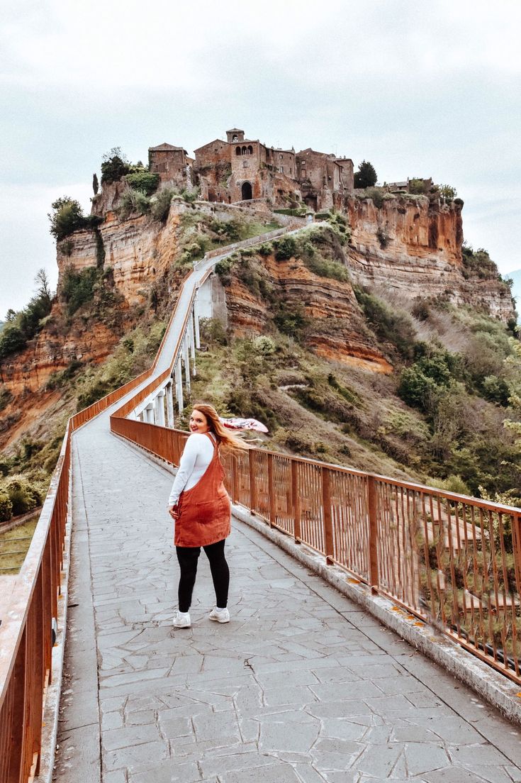 a woman in an orange dress is standing on a bridge with a castle in the background