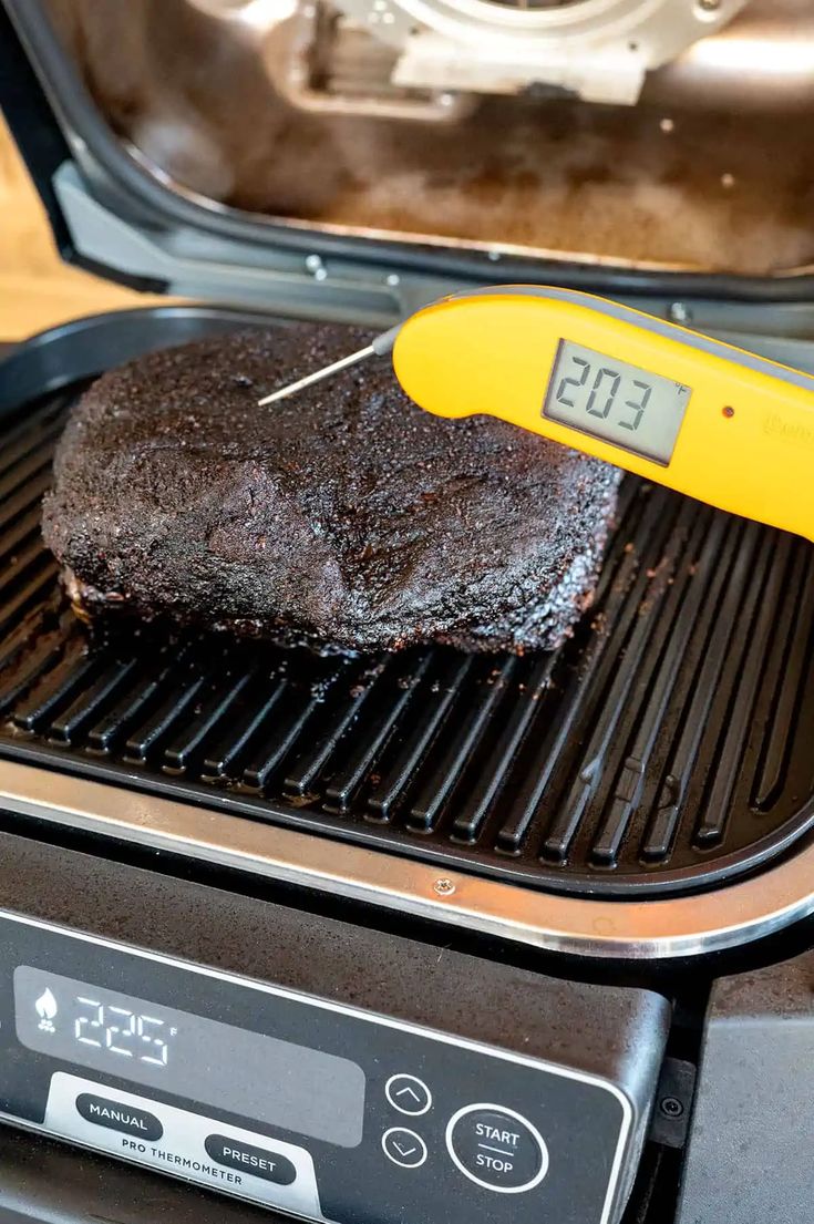 a piece of meat is being cooked on the grill with a digital thermometer