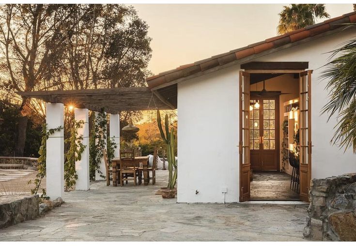 a small white house with an open patio and dining table in the front yard at sunset