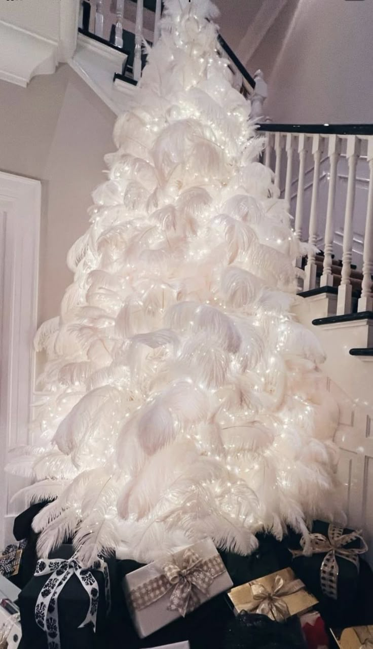 a white christmas tree decorated with feathers and presents under the bannister stair case