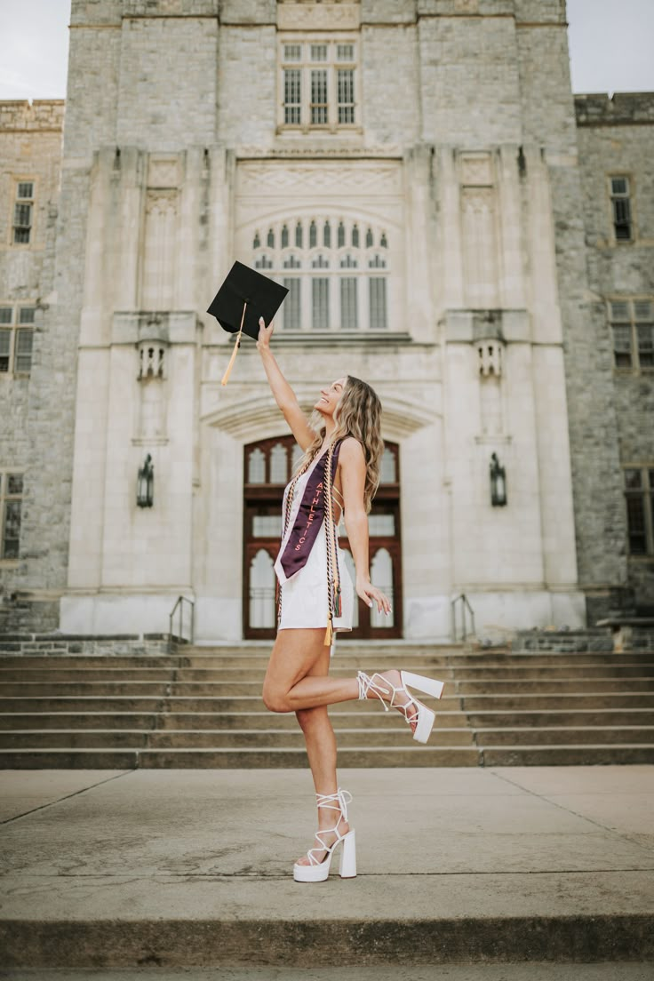 a woman in white dress holding up a black book and standing on steps outside a large building