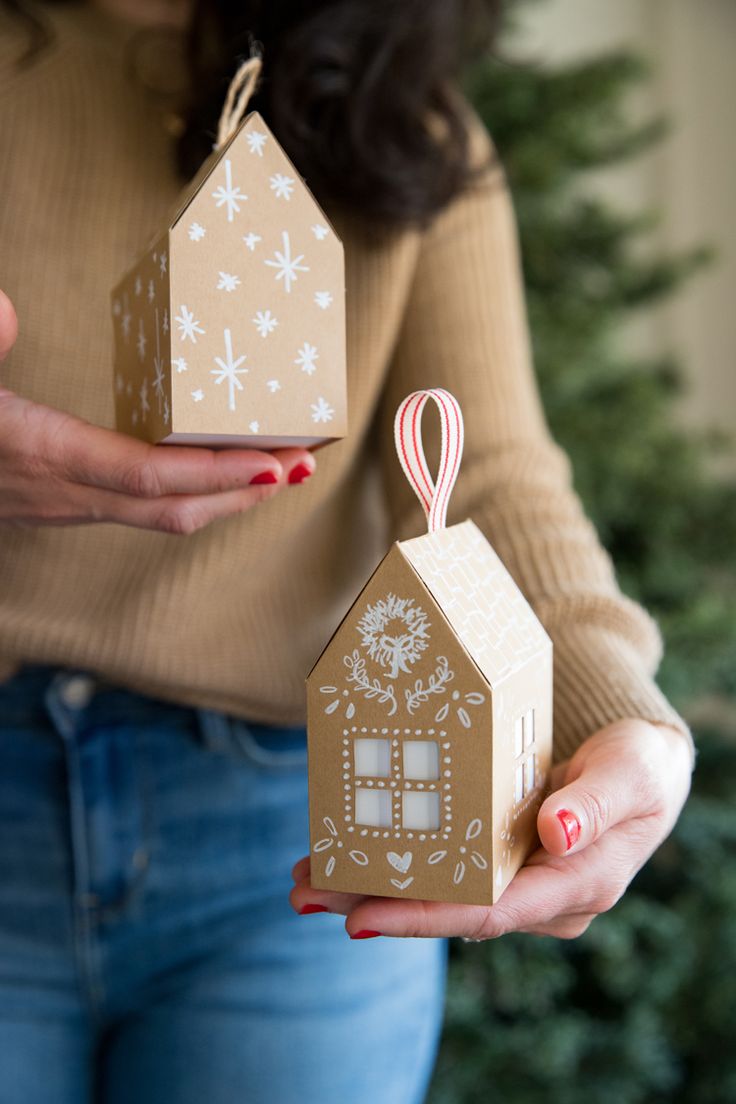 a woman holding two small boxes in front of a christmas tree with snowflakes on them