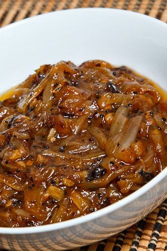 a white bowl filled with cooked onions on top of a woven table cloth next to a wooden spoon