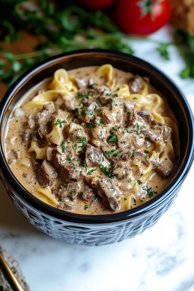 a close up of a bowl of food with pasta and meat in it on a table