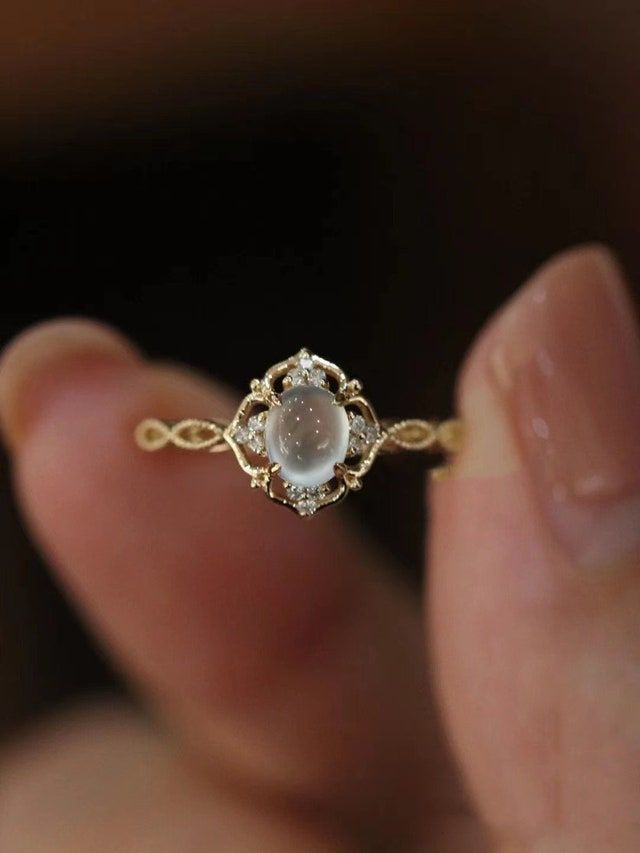 a woman's hand holding a gold ring with a white stone in the middle