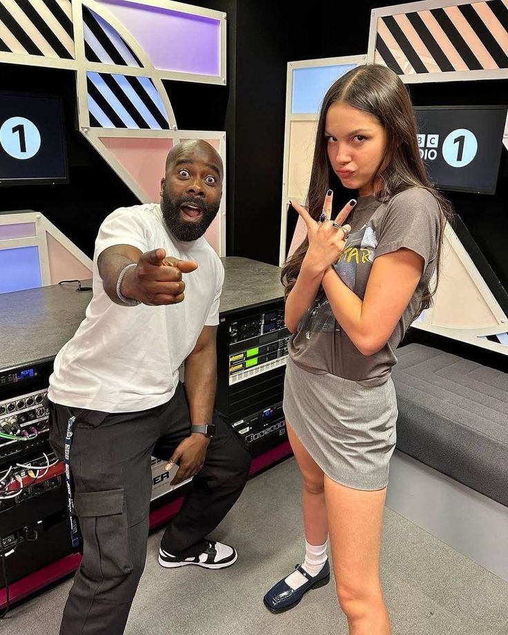 a man and woman standing in front of sound equipment with one hand up to the camera