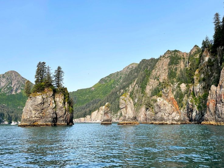 some very big rocks in the water by some mountains and trees on top of them