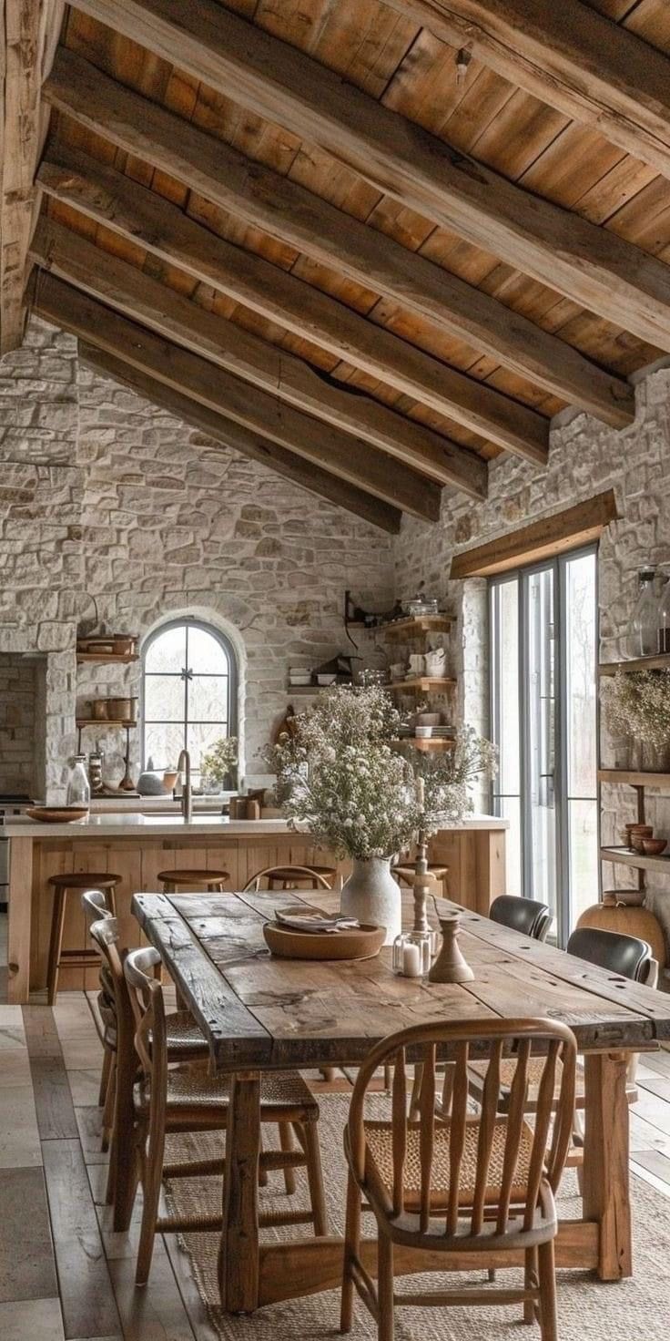 a rustic dining room with stone walls and exposed beams, wooden table surrounded by chairs