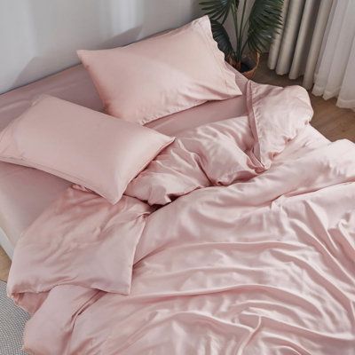 a bed with pink sheets and pillows next to a potted plant on the floor