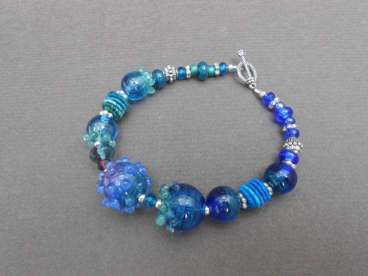 a blue beaded bracelet with glass beads and silver accents on a gray background,