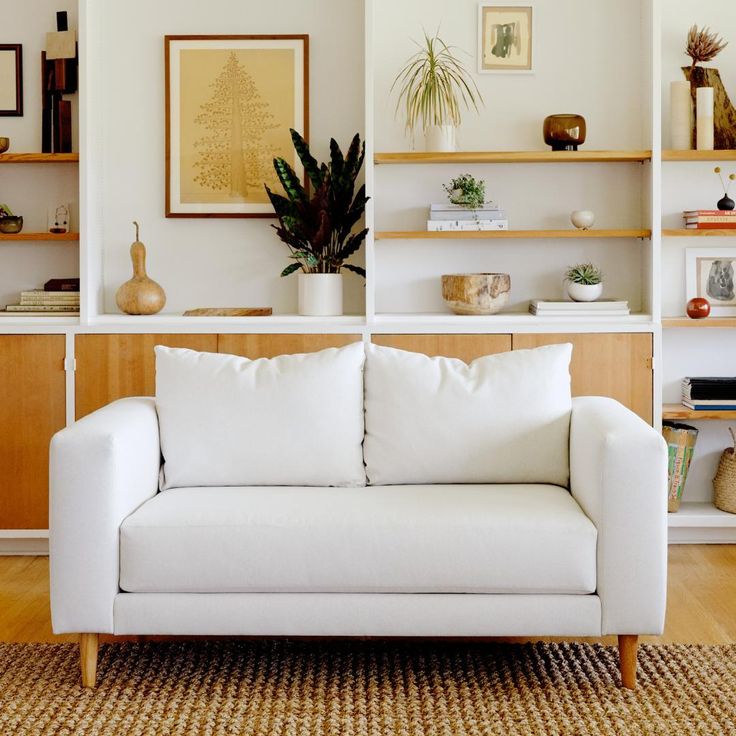 a white couch sitting on top of a wooden floor next to a shelf filled with books