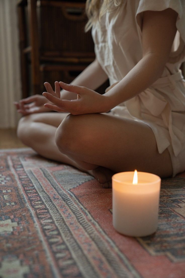 a woman sitting on the floor in front of a lit candle with her hands together