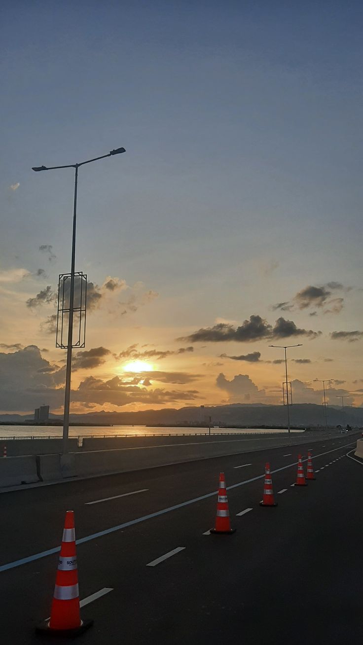 the sun is setting on an empty highway with traffic cones lined up along both sides