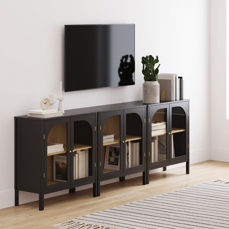 a tv mounted on the wall next to a book shelf with books and vases