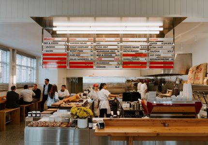 people are standing in the kitchen area of a fast food restaurant, with menus on the wall