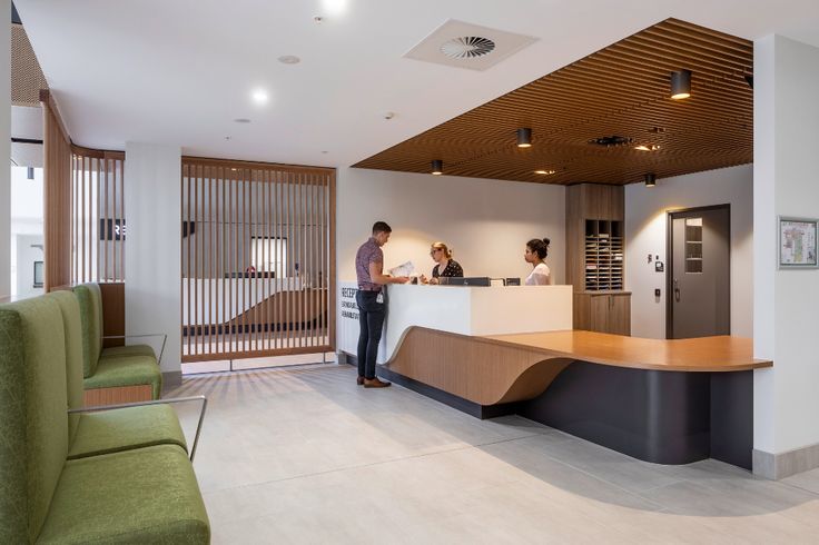 two people standing at the front desk of a modern hotel lobby with green couches