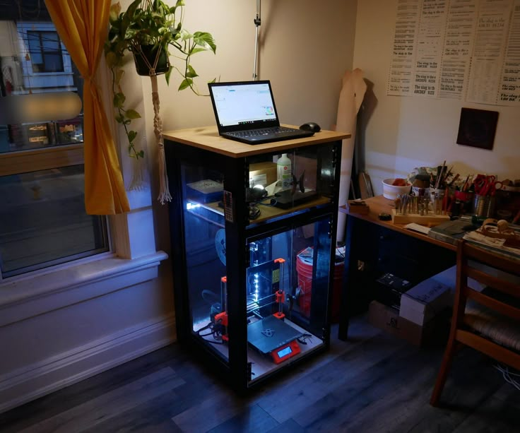 a laptop computer sitting on top of a glass case in front of a desk with a plant