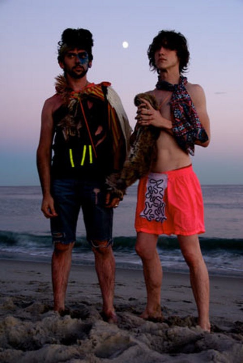 two men standing next to each other on top of a beach near the ocean at night