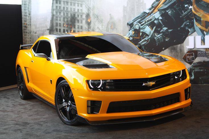 a yellow chevrolet camaro parked in front of a movie poster