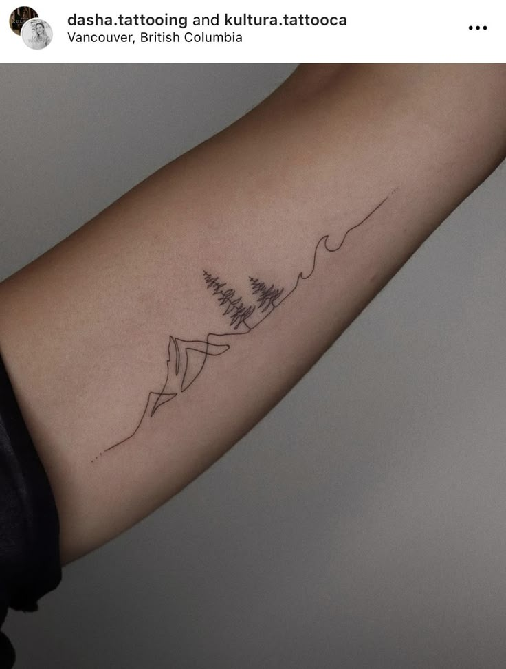 a person with a tattoo on their arm that has mountains and trees in the background