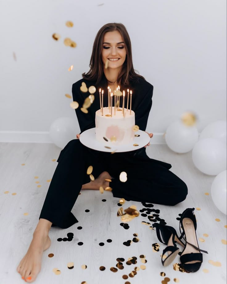 a woman sitting on the floor with a birthday cake in front of her and confetti falling around her