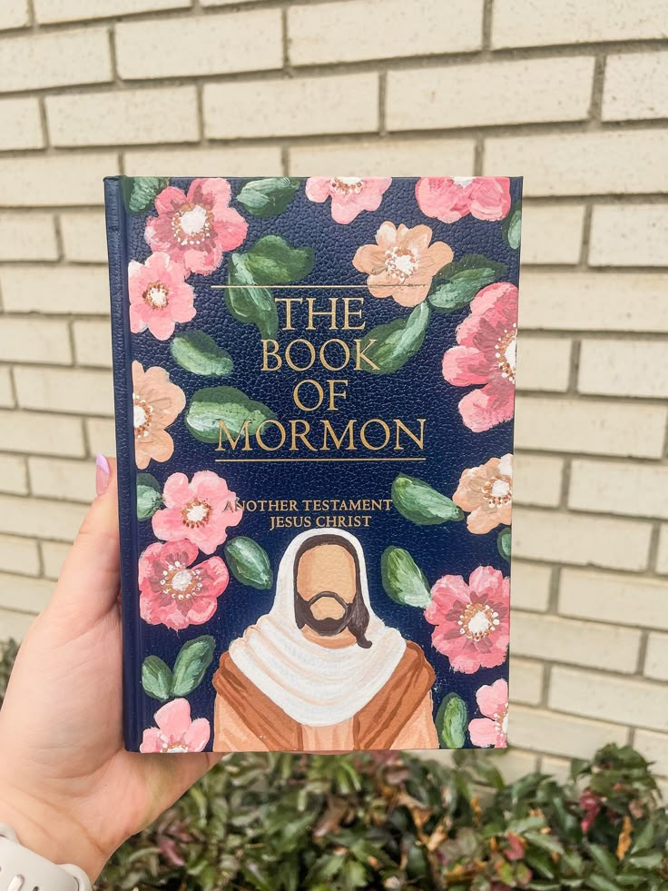 the book of mormon is held up in front of a brick wall with pink flowers