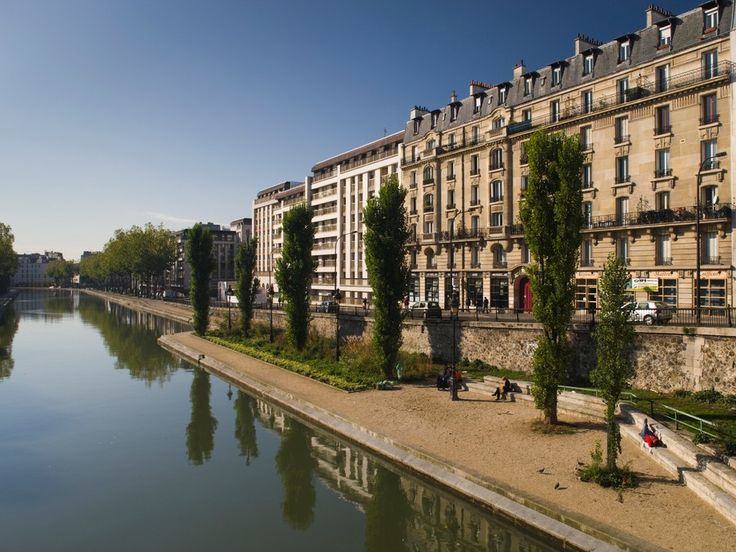 a river running through a city with tall buildings on both sides and trees growing along the bank