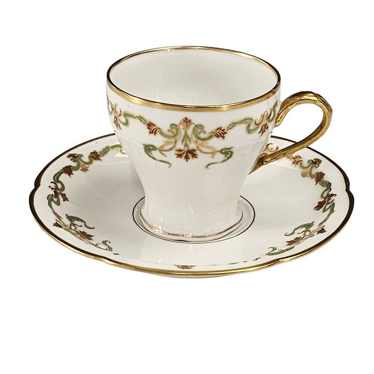 a white cup and saucer with gold trimming