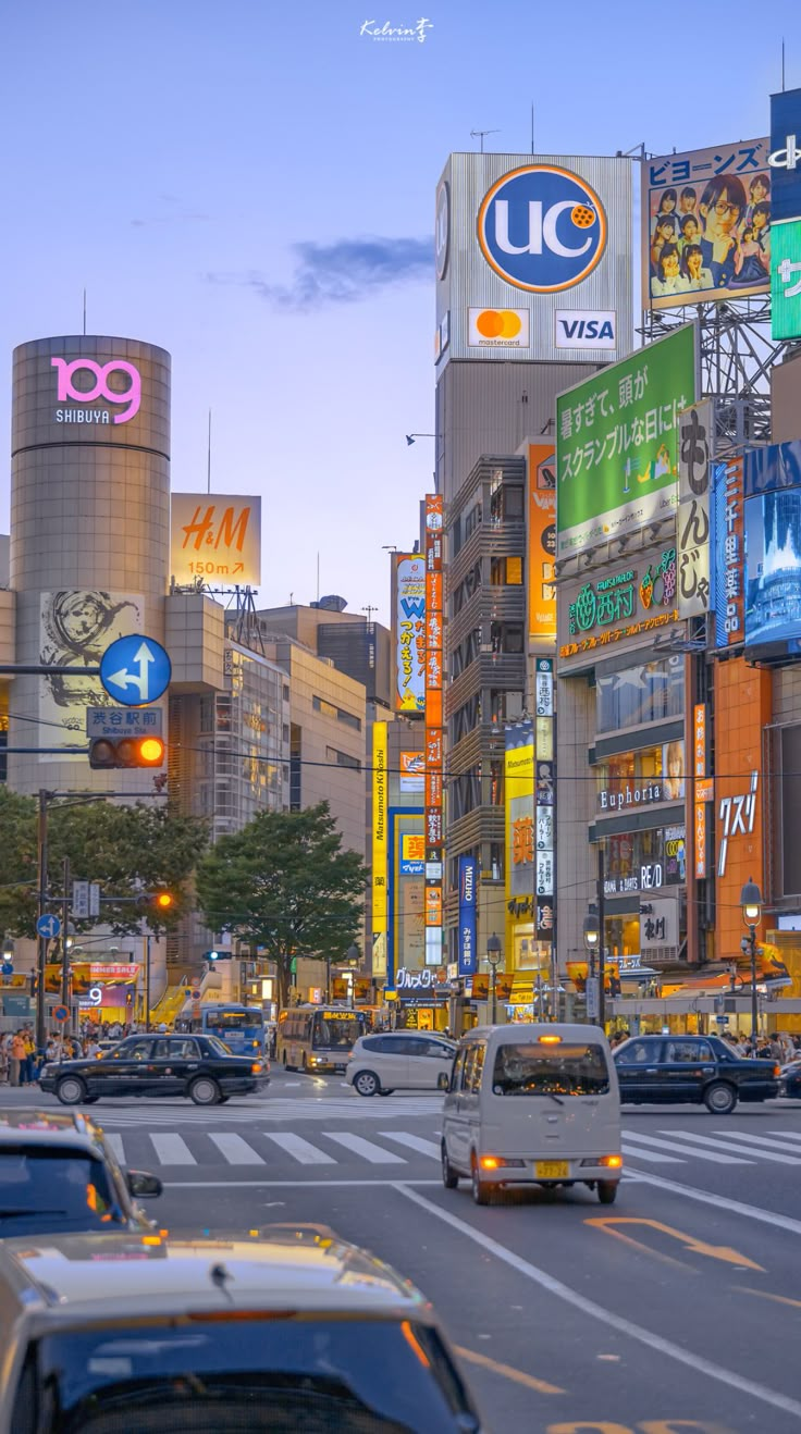 many cars are driving down the street in front of tall buildings with advertisements on them