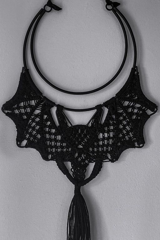 a black and white photo of a crocheted necklace hanging from a hook on a wall