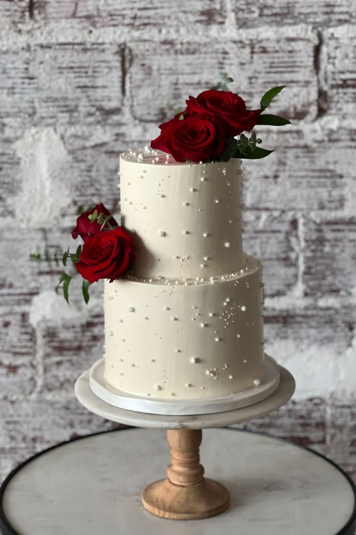 a three tiered white cake with red roses on top