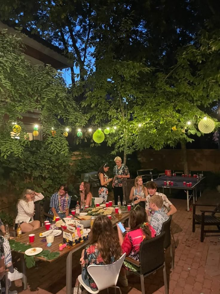 a group of people sitting around a table eating food and drinking beer at night time