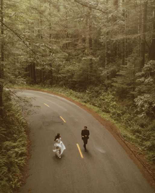 two people are walking down the road in the woods